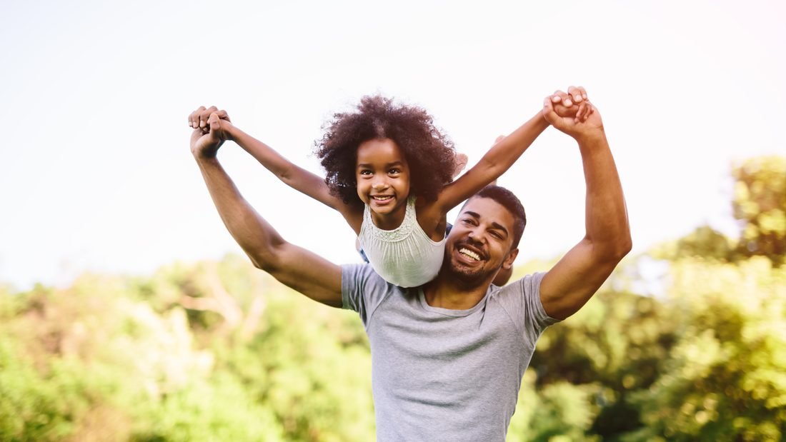 Padre con su hija sobre los hombros, celebrando juntos al aire libre